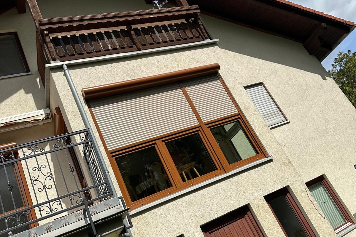 Hausfassade mit Holzbalkon und Fenstern in Holzdekor mit hellen Rollläden