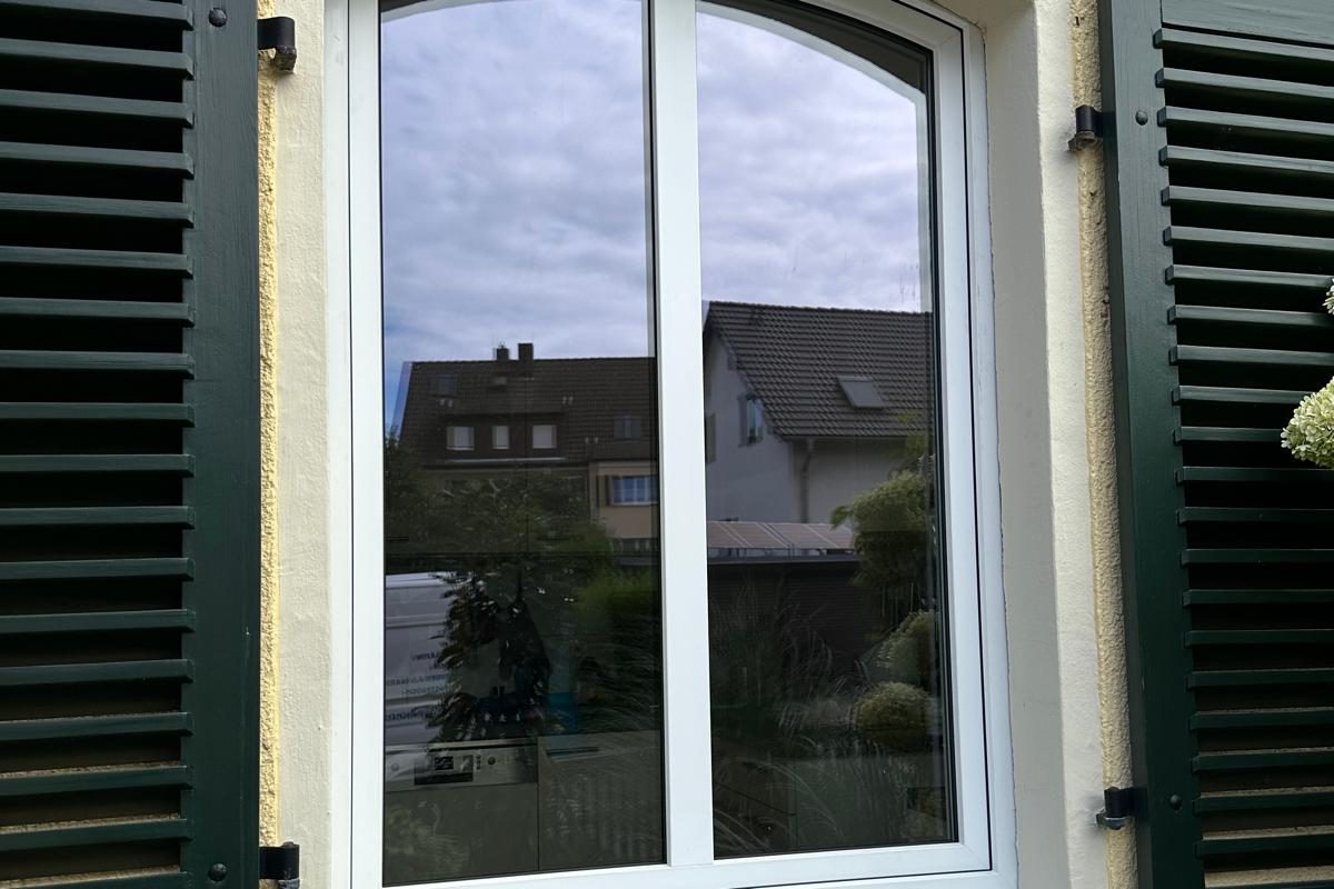 Weißes Rundbogenfenster zwischen dunkelgrünen Klappläden