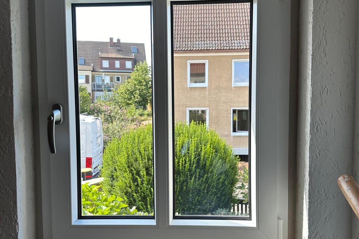 Weißes Fenster mit Blick in einen Garten mit Büschen