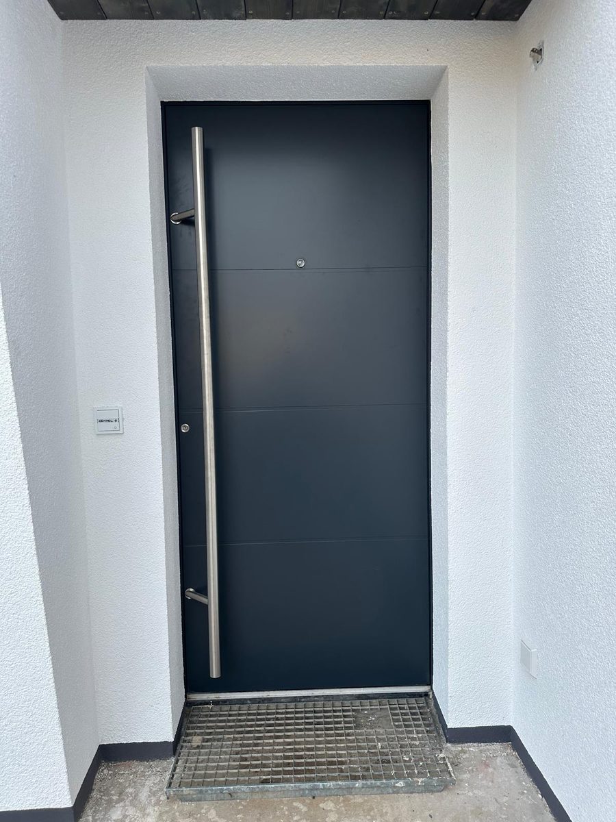 Anthrazitfarbene Haustür mit langem Edelstahl-Stoßgriff und Fußmatte