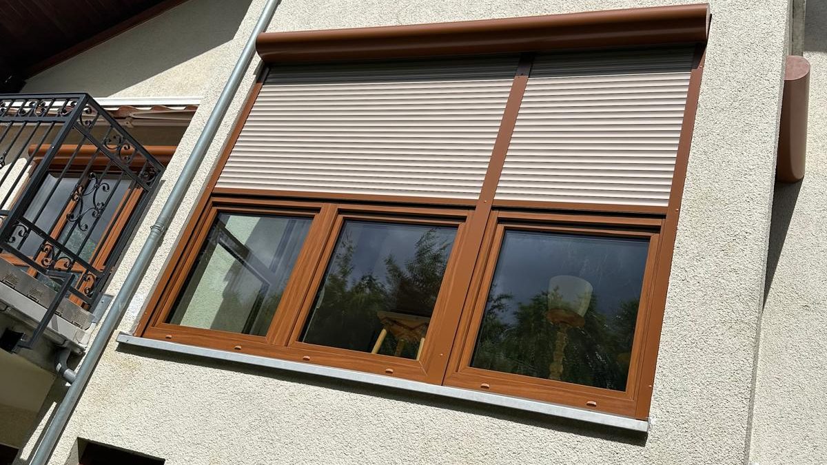 Fenster in Holzdekor mit hellen Rollläden an einer Putzfassade