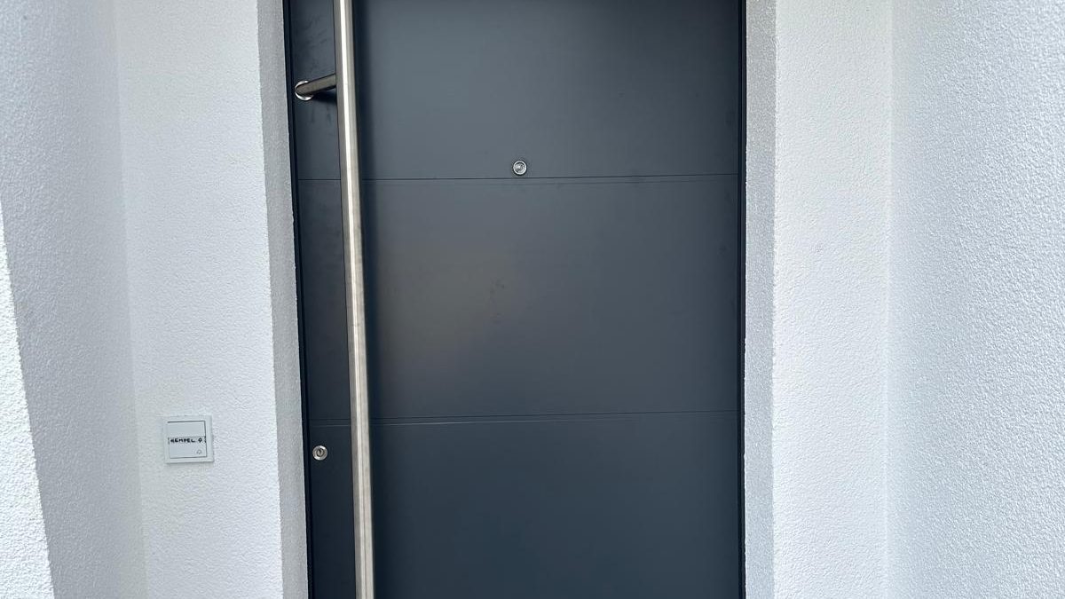 Anthrazitfarbene Haustür mit langem Edelstahl-Stoßgriff in einem weißen Eingang