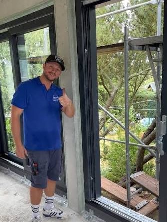 Sebastian Weinhold in blauem Firmenshirt vor neu eingebauten Fenstertüren